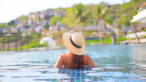 Primer-Plano,-De-Vuelta-A-La-Cámara,-Una-Mujer-Joven-En-Una-Piscina-Mirando-La-Ciudad-Turística-Encaramada-En-El-Borde-De-Una-Montaña