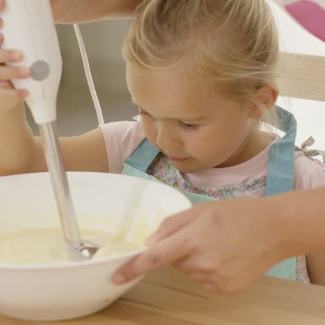 cute little girl learning to bake from mother