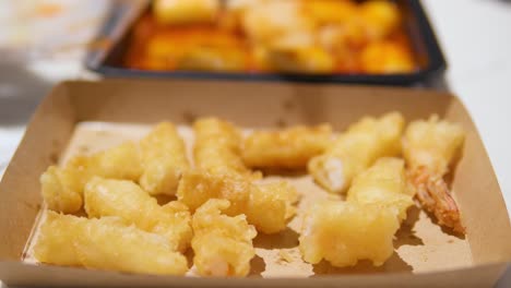 woman's hand picks korean traditional street food crispy fried shrimp tempura from paper single-use bowl