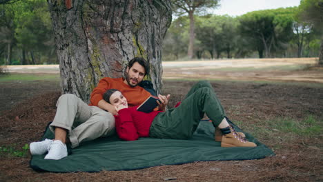 relaxed couple lying picnic blanket tree vertically. man reading book to woman