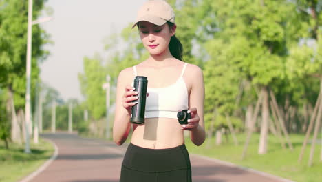 Retrato-De-Una-Hermosa-Atleta-Tomando-Un-Descanso-Durante-La-Carrera-Para-Hidratarse-Haciendo-Ejercicio,-Deportista-Con-Ropa-Deportiva-Bebiendo-Agua-De-Una-Botella-Mientras-Hace-Ejercicio-En-Un-Parque-Público-Por-La-Mañana