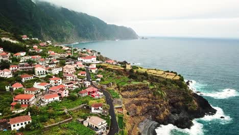 aerial view capturing seixal, a charming village on the north rugged coastline of madeira island, featuring traditional red-roofed houses, lush hillsides, and dramatic cliffs, drone establishing shot