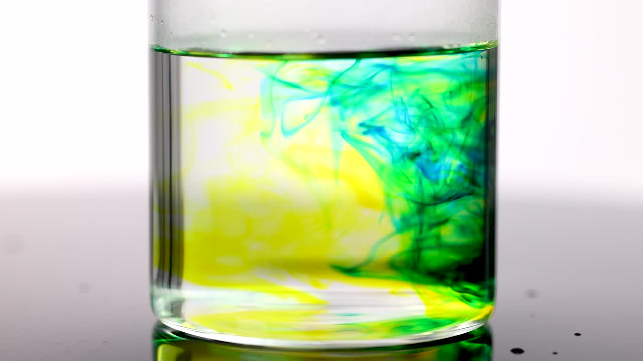 Blue and yellow dye dispersing in clear water, high-key lighting, static camera, macro shot