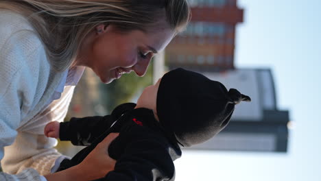 happy mom tossing her little baby. infant wearing black suit smiles to mother and then frowns. close up. vertical screen.