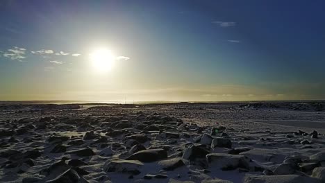 Aerial-of-rocky,-snowy-terrain-in-Keflavik,-Iceland-in-winter,-flying-towards-the-distant-shore