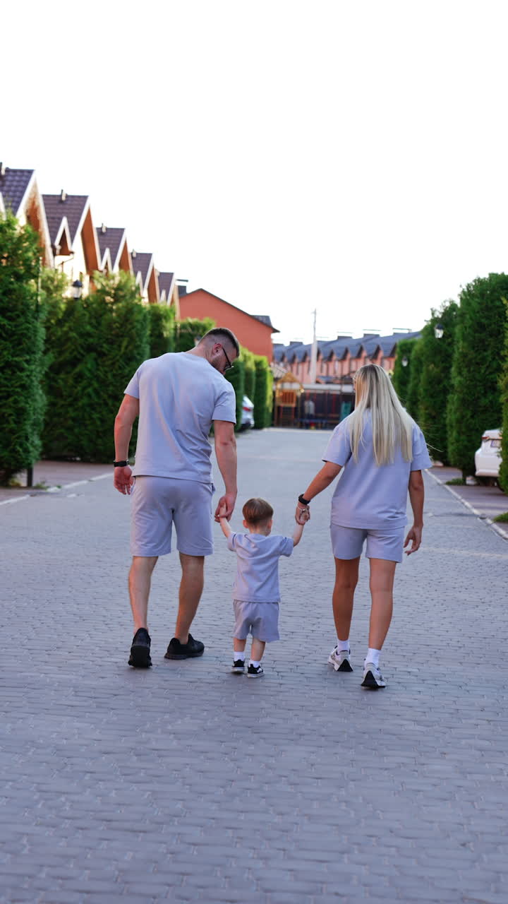 Family of three wearing similar shorts and t-shirts walk away from camera. Happy mom and dad with baby on the walk outdoors. Vertical video