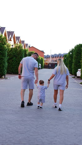 Family of three wearing similar shorts and t-shirts walk away from camera. Happy mom and dad with baby on the walk outdoors. Vertical video