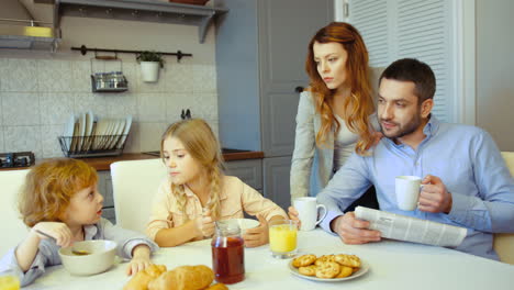 a mother having coffee in the kitchen while her husband talks to their kids