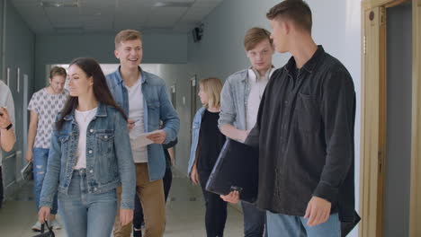 many people walk down the hall of the university during the break between classes talking to each other and laughing. everyday communication in college.