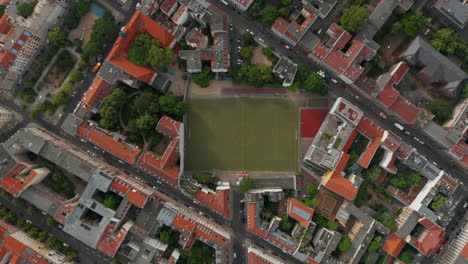 Aerial-birds-eye-overhead-top-down-view-of-urban-neighbourhood-with-football-playground.-Ascending-shot-of-streets-with-buildings.-Berlin,-Germany.