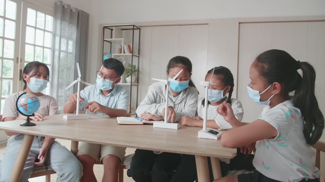 Middle School Classroom: Asian Kids Are Wearing Facemasks Learning About Ecology Problems And Their Solution With Wind Turbine Model And Globe At School
