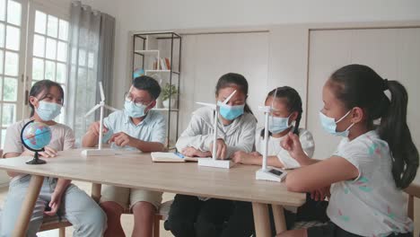 middle school classroom: asian kids are wearing facemasks learning about ecology problems and their solution with wind turbine model and globe at school