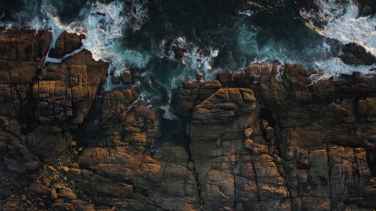 Foamy Sea Waves Crashing On Rocky Shore At Sunset - aerial top down