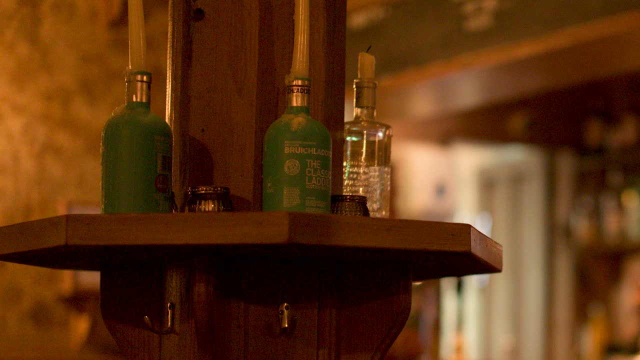 Warmly lit wooden shelf with whisky bottles in traditional Scottish pub, shallow focus, static shot
