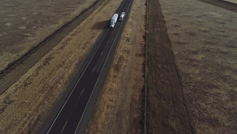 Drone-shot-of-trucks-passing-on-desolate-highway