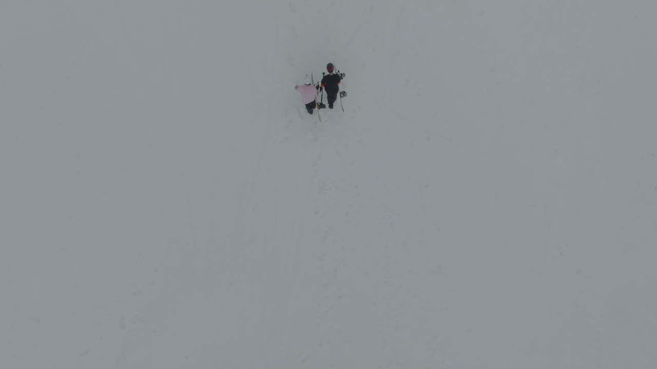 Drone view above two snowboarders holding snowboards and walking uphill the pistes on the snowy slopes of Mount Hermon, Golan Heights, Israel