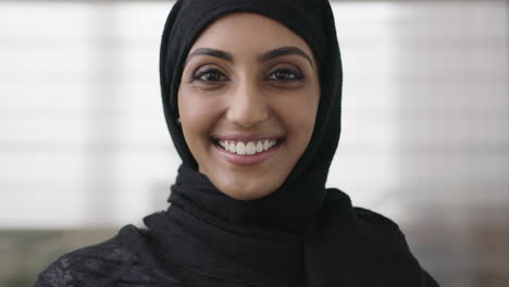 close-up-portrait-of-professional-young-muslim-business-woman-looking-at-camera-smiling-happy-wearing-traditional-headscarf-in-office-background