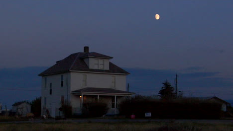 the moon rises over a two story house in the countryside