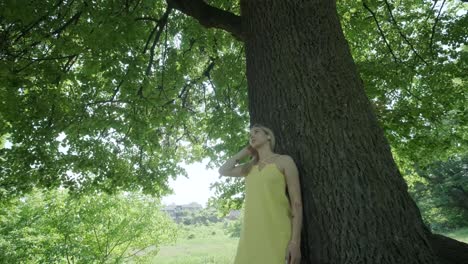 woman in yellow dress dancing by tree in summer park