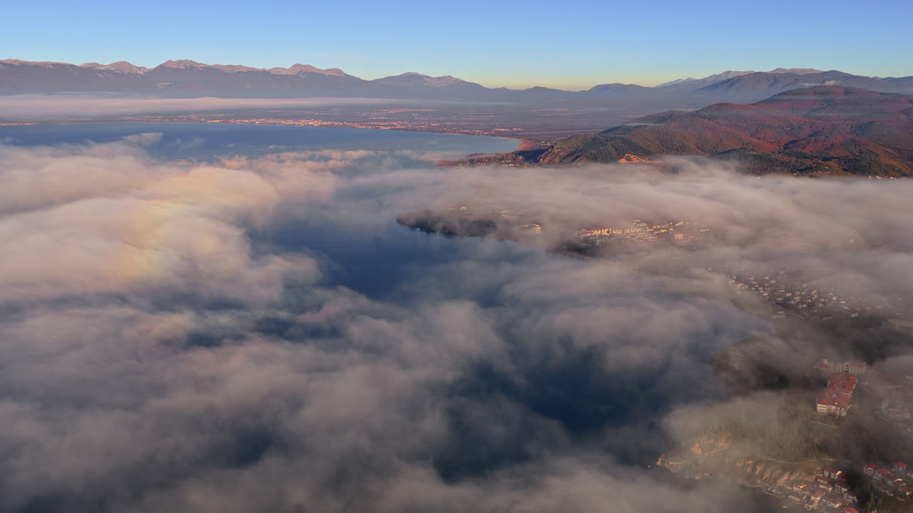 Aerial drone view of a Galichica mountain ridge rising above a sea of clouds, with soft layers of fog covering the valley below