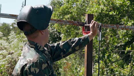 slow motion welder takes away clamp from plank at fence