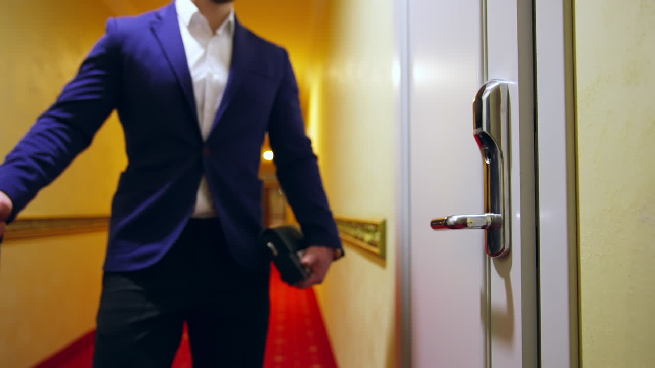 Businessman with a baggage in a hotel. Young man in elegant clothes comes to the door of his room in the hotel and opens it. Slow motion.