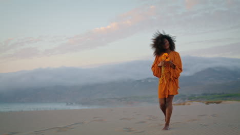 una mujer sonriente disfruta de un ramo caminando por las dunas de arena en una sombría noche de verano.
