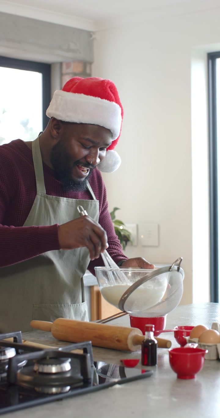 Vertical video: African American man at counter sieving flour into bowl, whisking Christmas batter