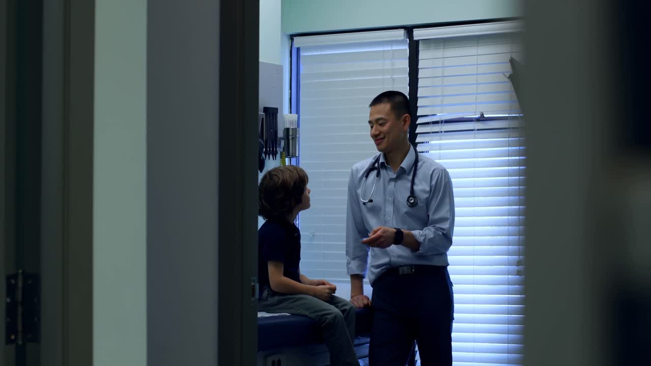 vista frontal de un joven médico asiático que muestra un modelo de oreja a un paciente caucásico en la clínica 4k