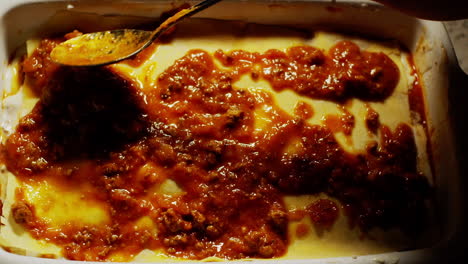 extendiendo la salsa boloñesa con una cuchara durante la preparación de una lasaña