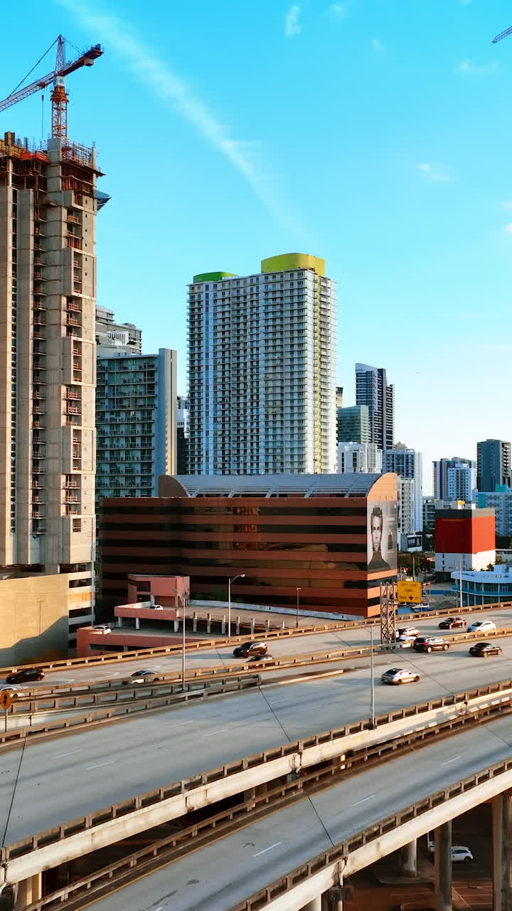 Two construction sites of the multi-storied buildings in the city downtown. Multiple cars run by the freeway of Miami, Florida, USA. Vertical video
