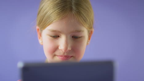 retrato de estudio de una niña usando una tableta digital contra un fondo púrpura