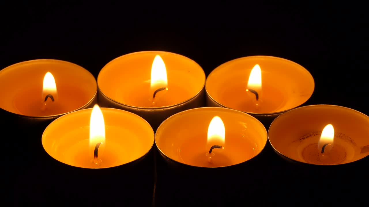 The candle flickers in the dark. A white round candle burns on a dark background. Round candles burn and go out. Sorrow. Romance. Joy. 4K video