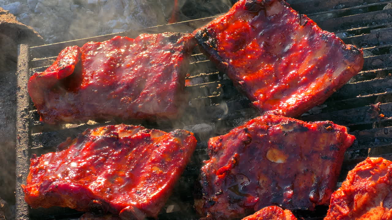 cocinar jugosas costillas de cerdo a la parrilla en una parrilla de fuego al aire libre con humo y cenizas, carne deliciosa, tiro de 4k