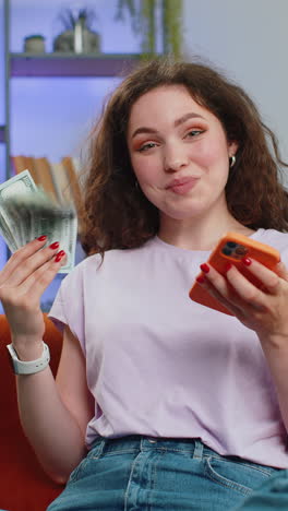 mujer joven sonriente feliz contando dinero en efectivo uso de teléfono inteligente ingresos ahorra lotería ganar presupuesto en casa