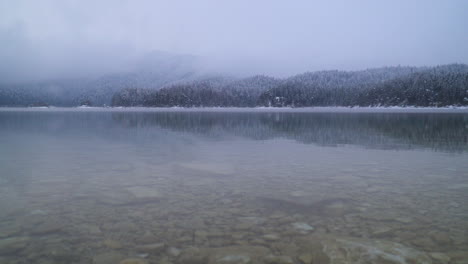 Bosques-Etéreos-Nevados-Y-Brumosos-Reflejos-En-La-Costa-Del-Lago-Eibsee,-Baviera