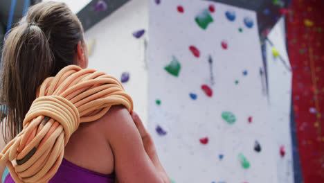 Vista-Trasera-De-Una-Mujer-Caucásica-Con-Una-Cuerda-Sobre-Su-Hombro-En-Un-Muro-De-Escalada-Interior.