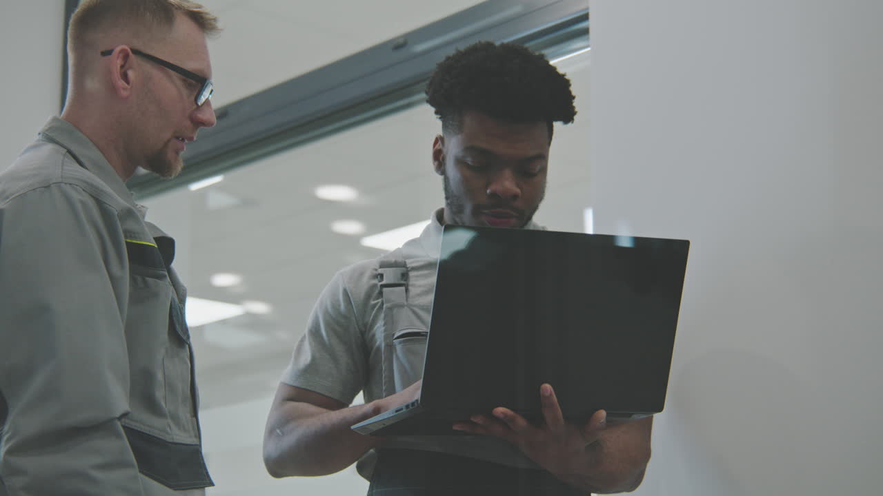 Two Workers Discussing Project on a Laptop in a Modern Factory