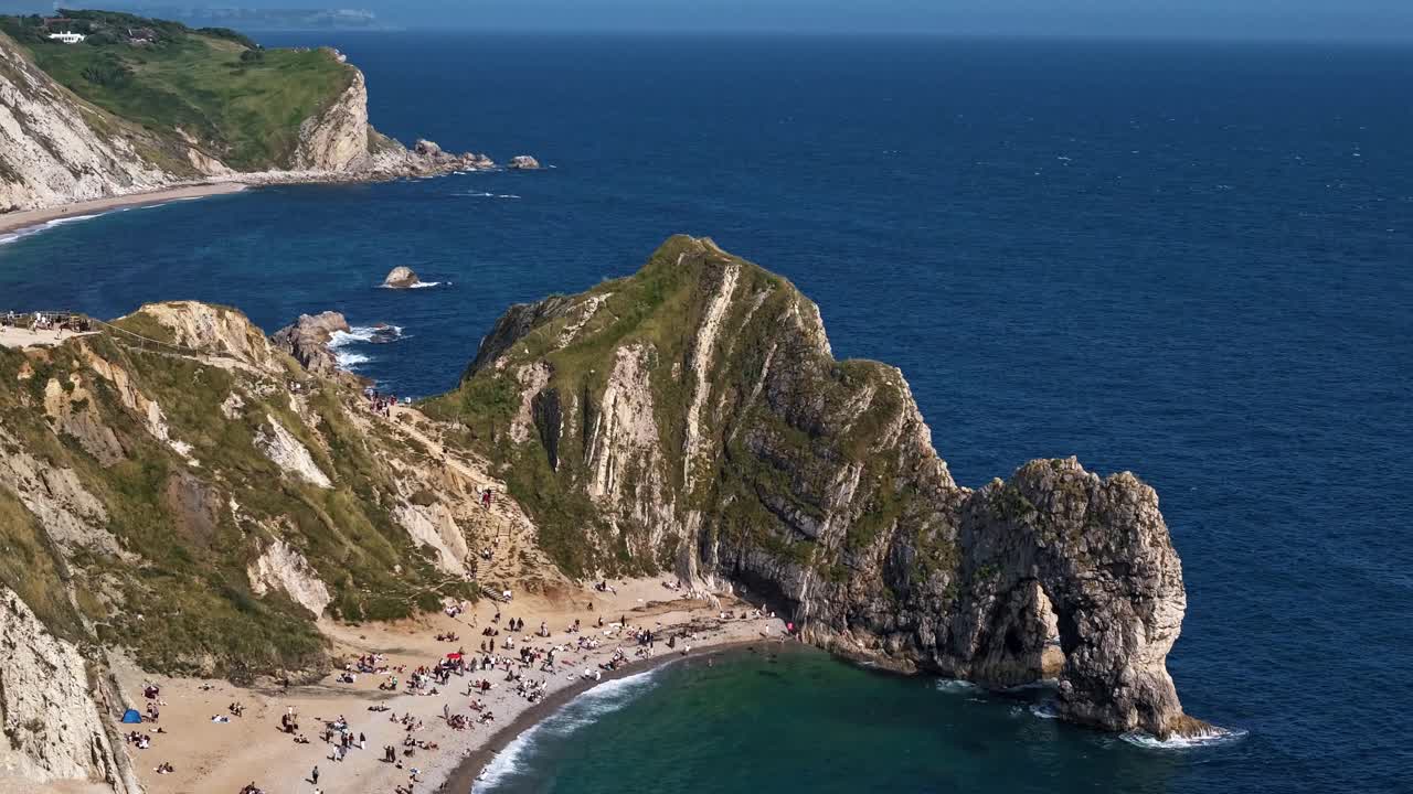 Timelapse da costa de Durdle Door, pessoas explorando a praia enquanto a luz se move sobre o arco marinho e o penhasco