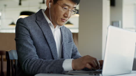 man in glasses typing on laptop computer and listening to music or radio through earphones