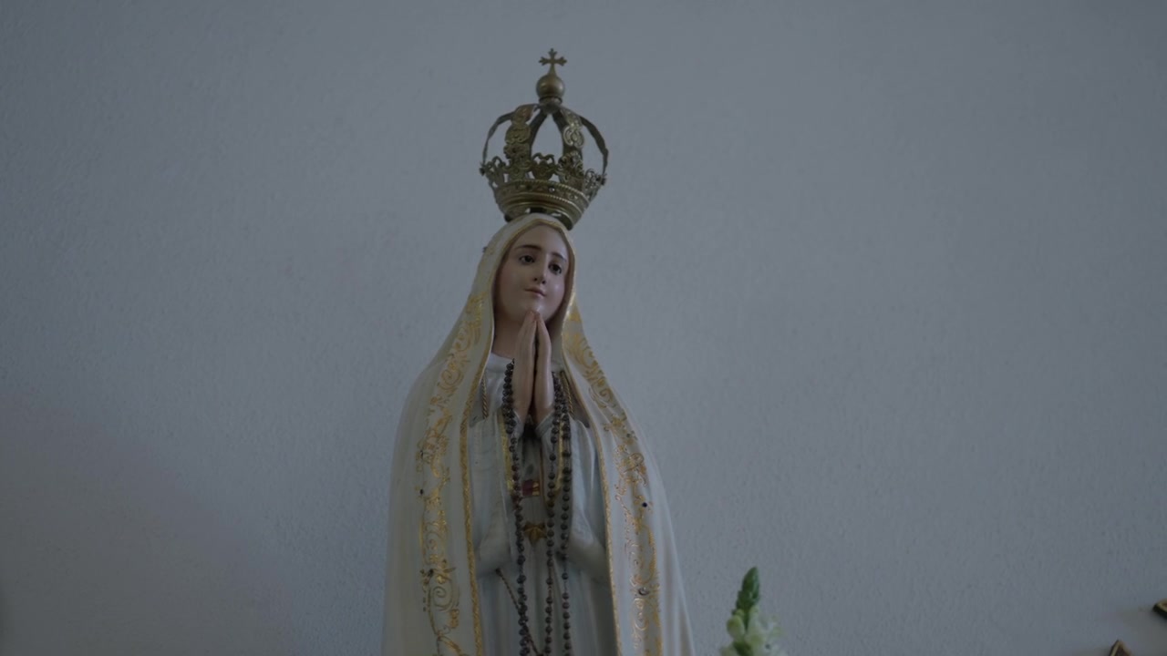 Statua della Madonna di Fatima incoronata d'oro con rosario e mani giunte in preghiera all'interno di una cappella.