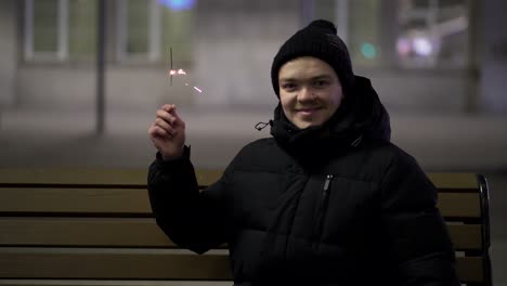 young man with sparkler on a bench at night