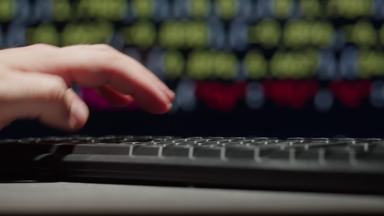 persona escribiendo en un teclado de computadora frente a una pantalla de datos del mercado de valores