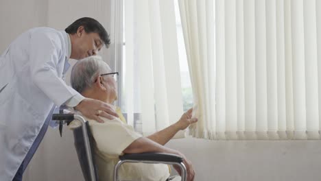 doctor and old asian man sits in a wheelchair and looks out the window. health care and insurance, retirement concept