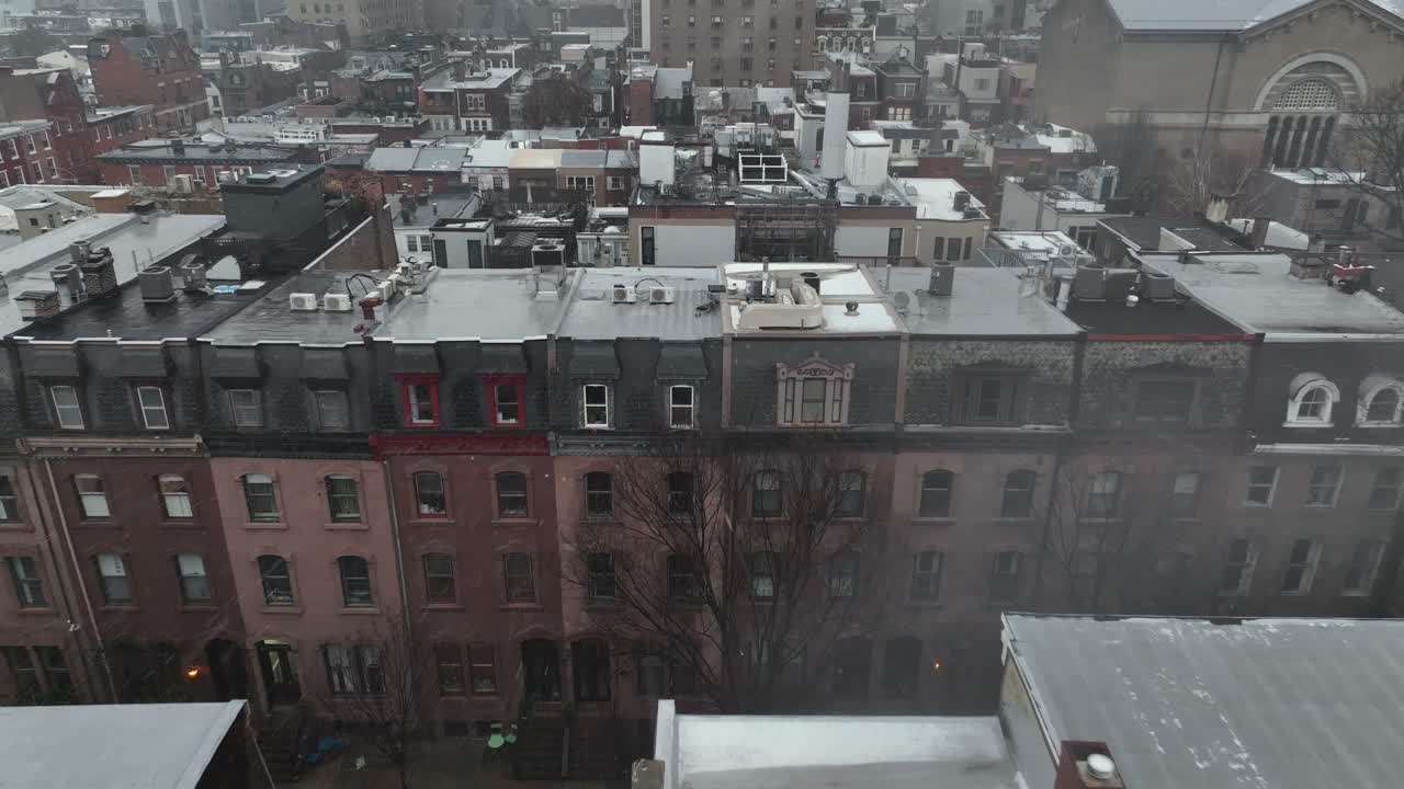 Aerial approaching shot of snow-covered residential neighborhood near downtown Philadelphia, showing dense row houses, rooftops dusted with snow and overcast winter atmosphere. Low income townhouses