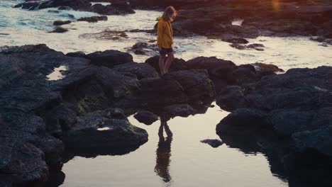 windy shoreline sunset – japanese ocean scene
evening sun lights up clouds and waves while a woman looks to sea, still and serene on rugged coastal rocks.