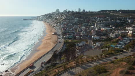 Aerial-view-passing-official-Republic-of-Chile-flag-flying-on-Reñaca-hillside-following-coastal-road-to-downtown-city