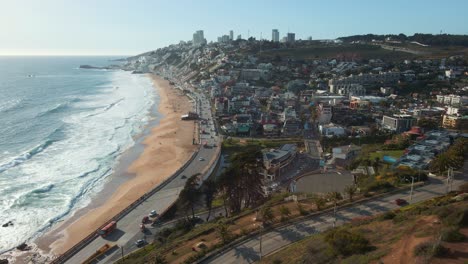aerial view passing official republic of chile flag flying on reñaca hillside following coastal road to downtown city