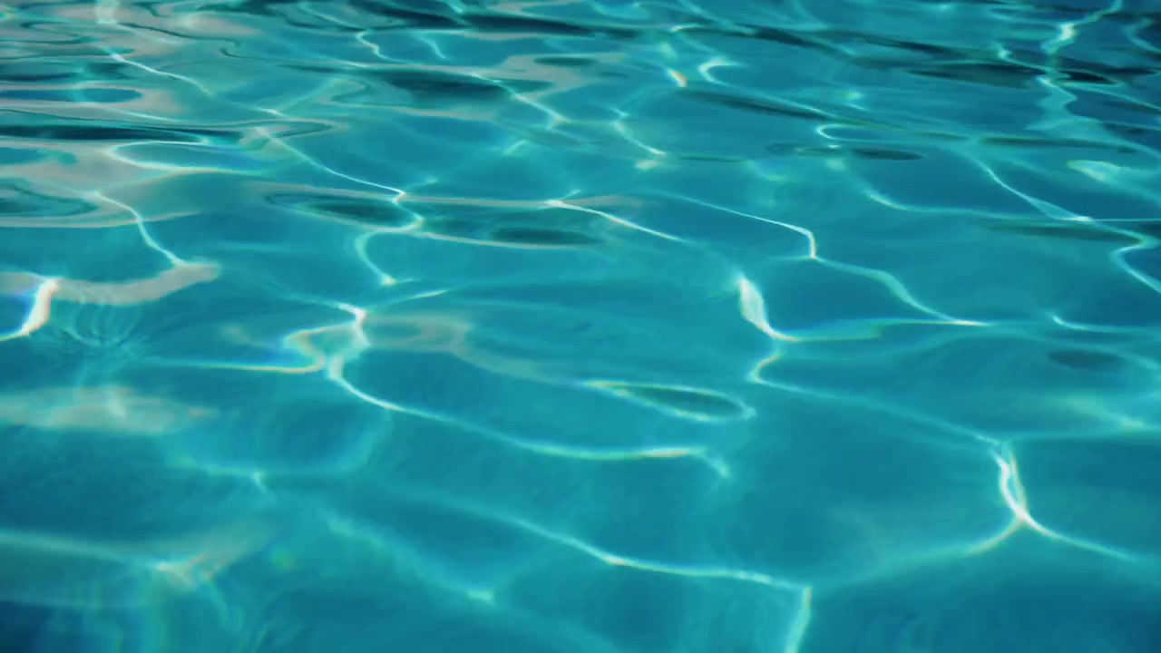 Pemandangan close-up air kolam renang biru cerah jernih dengan riak lembut sinar matahari
