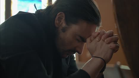 young man in black suit praying in church pew in cinematic slow motion with folded hands